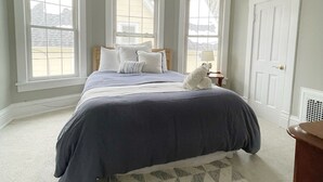 Quarto com uma cama grande, duas janelas, uma porta e um tapete.