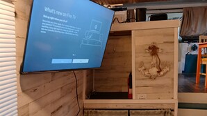 A room with a mounted TV displaying a guide, wooden walls, a wooden cabinet, and a curtain. - Classic  2-bedroom , cabin yacht ,house boat ,in the bayou Springfield La (Springfield)