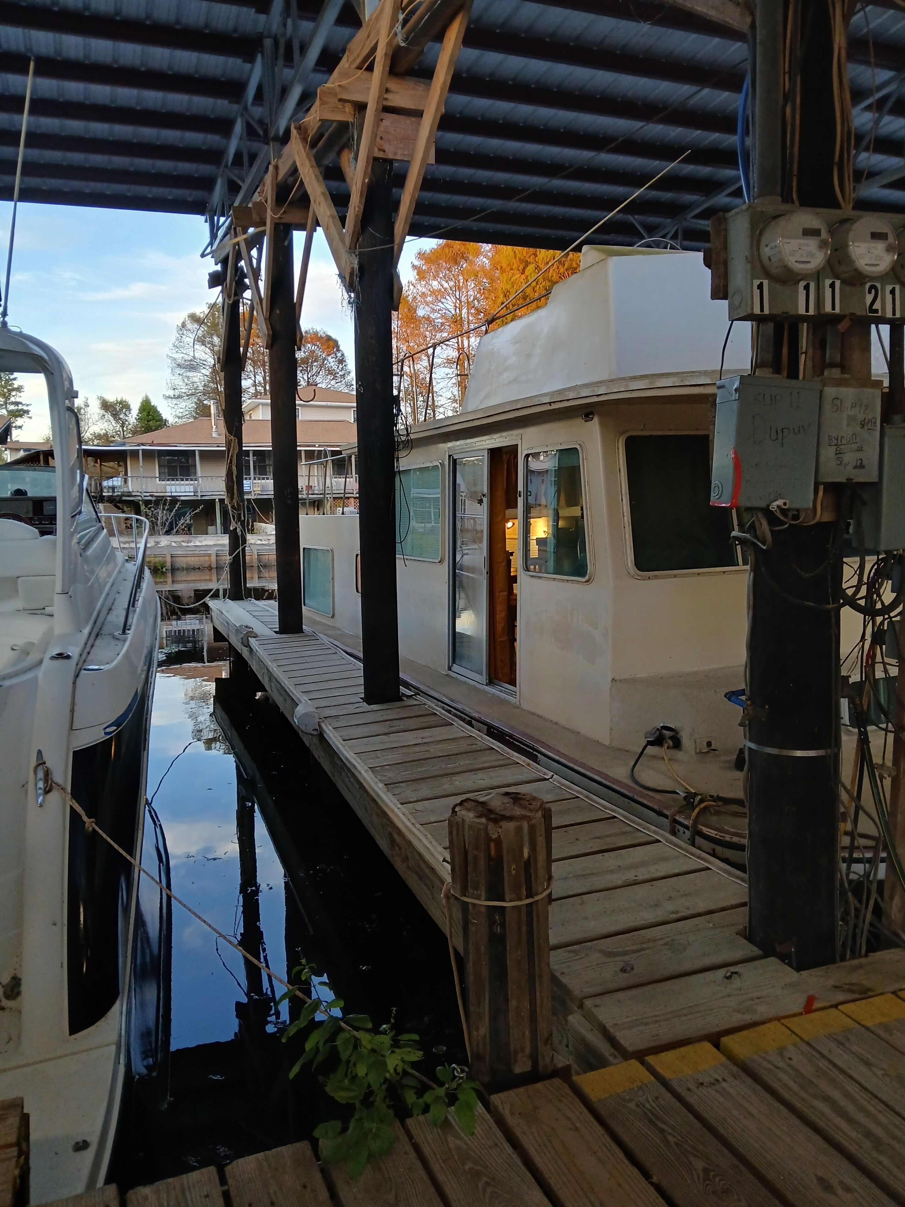 A docked houseboat with a wooden deck, a small window, and electrical panels.