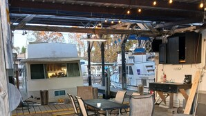 An RV park with a covered outdoor area featuring a table and chairs, a bar stool, and a grill. - Classic  2-bedroom , cabin yacht ,house boat ,in the bayou Springfield La (Springfield)