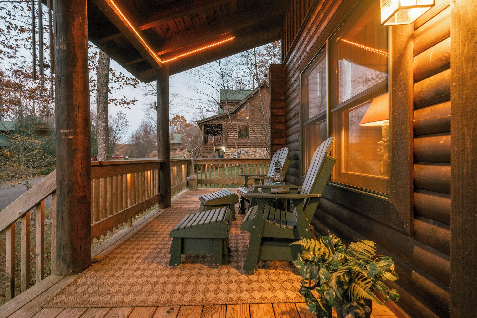 A wooden cabin with a porch, two Adirondack chairs, a small table, and a potted plant.