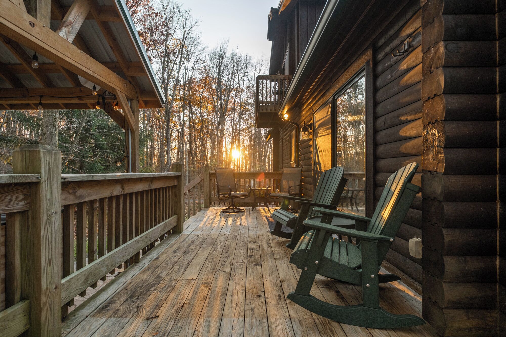 A wooden deck with rocking chairs and a table, overlooking a forested area.