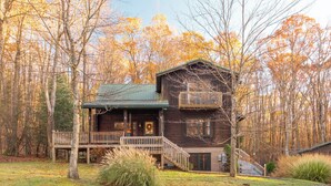 A two-story log cabin with a balcony, surrounded by a forest. - Pine Loom Lodge ~ Minutes to Golf, Lake & Wisp; Hot Tub, Game Room (Oakland)