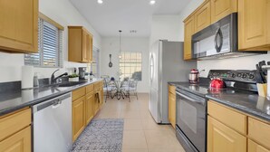A modern kitchen with wooden cabinets, stainless steel appliances, and a dining area with a table and chairs. - 3BR w patio, community pool, dog friendly (Chandler)
