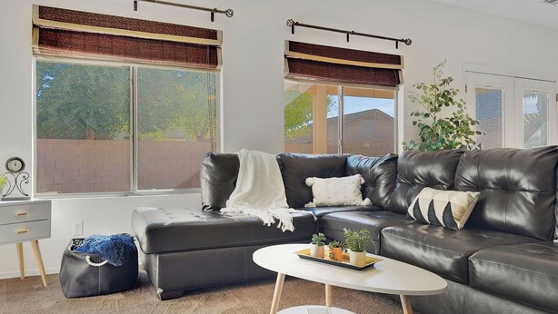 A modern living room with a black leather sofa, a white coffee table, and a large window with blinds. - 3BR w patio, community pool, dog friendly (Chandler)