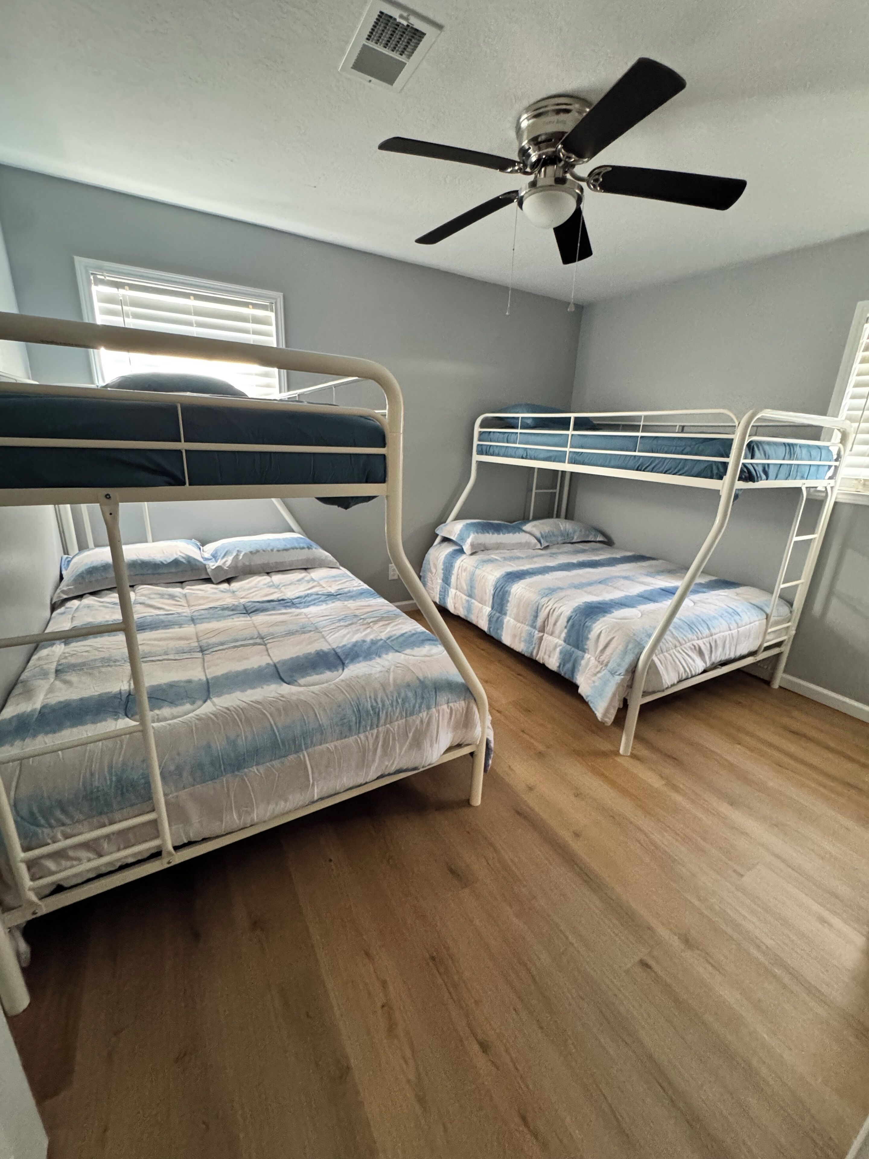 A room with two bunk beds, a ceiling fan, and a window with blinds.