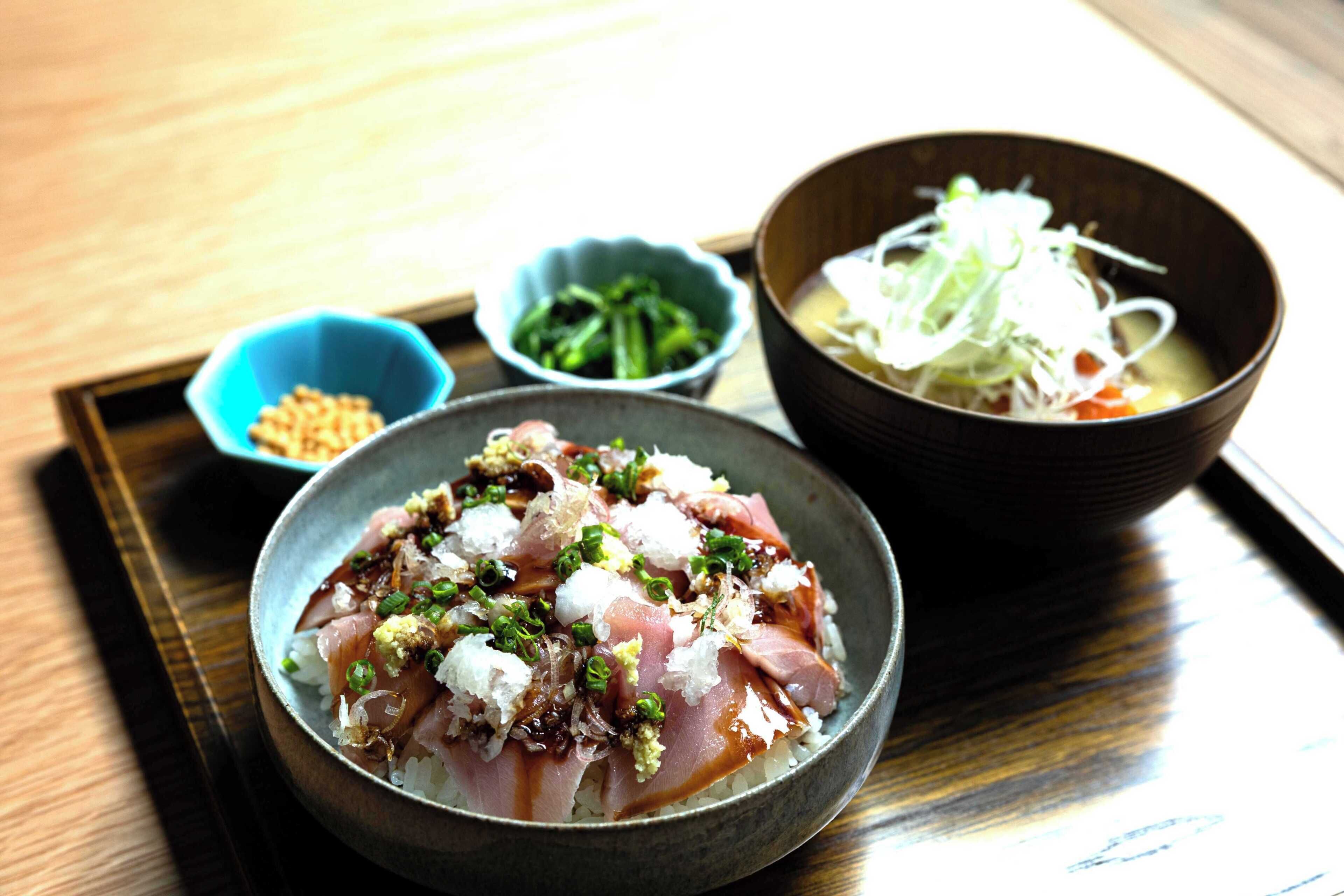 A meal with sashimi, rice, and a soup bowl on a tray.