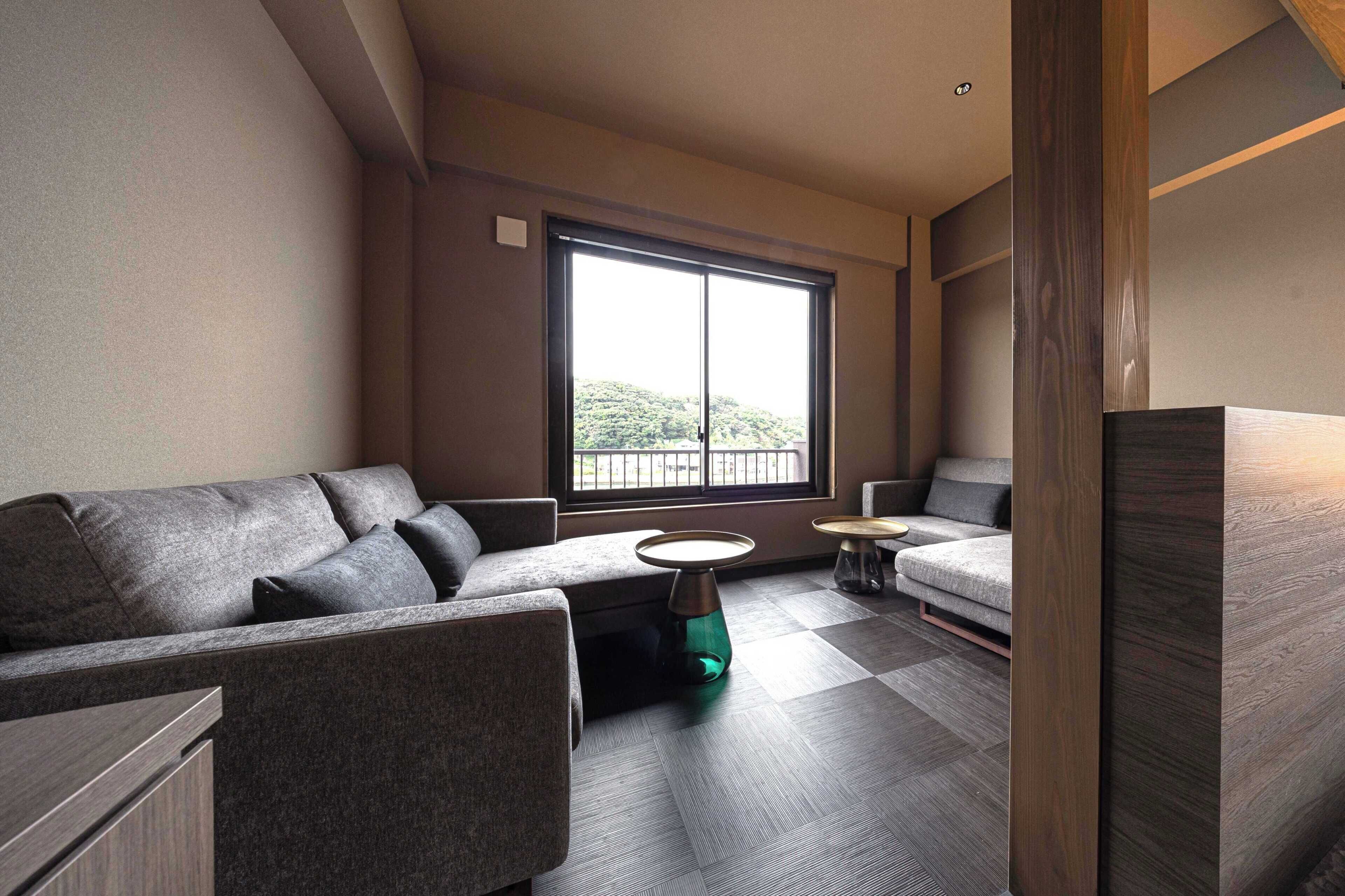 A modern living room with a sofa, a coffee table, and a small side table. A large window provides a view of greenery outside.