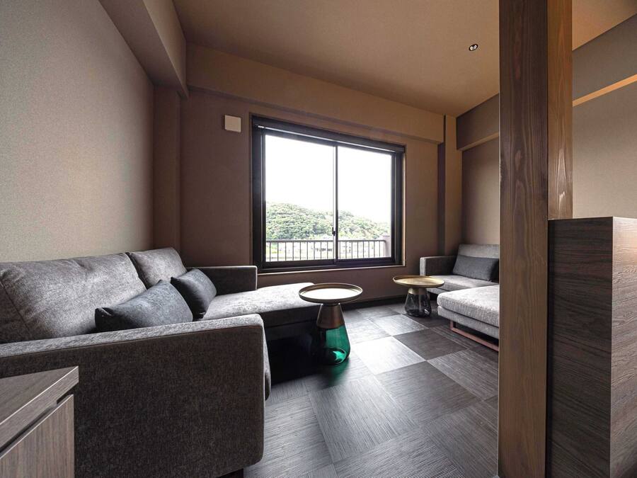 A modern living room with a sofa, a coffee table, and a small side table. A large window provides a view of greenery outside.