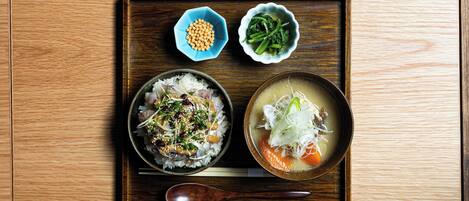 A wooden tray with a bowl of rice topped with vegetables and sesame seeds, a bowl of soup with noodles and vegetables, and two small bowls containing soybeans and greens.
