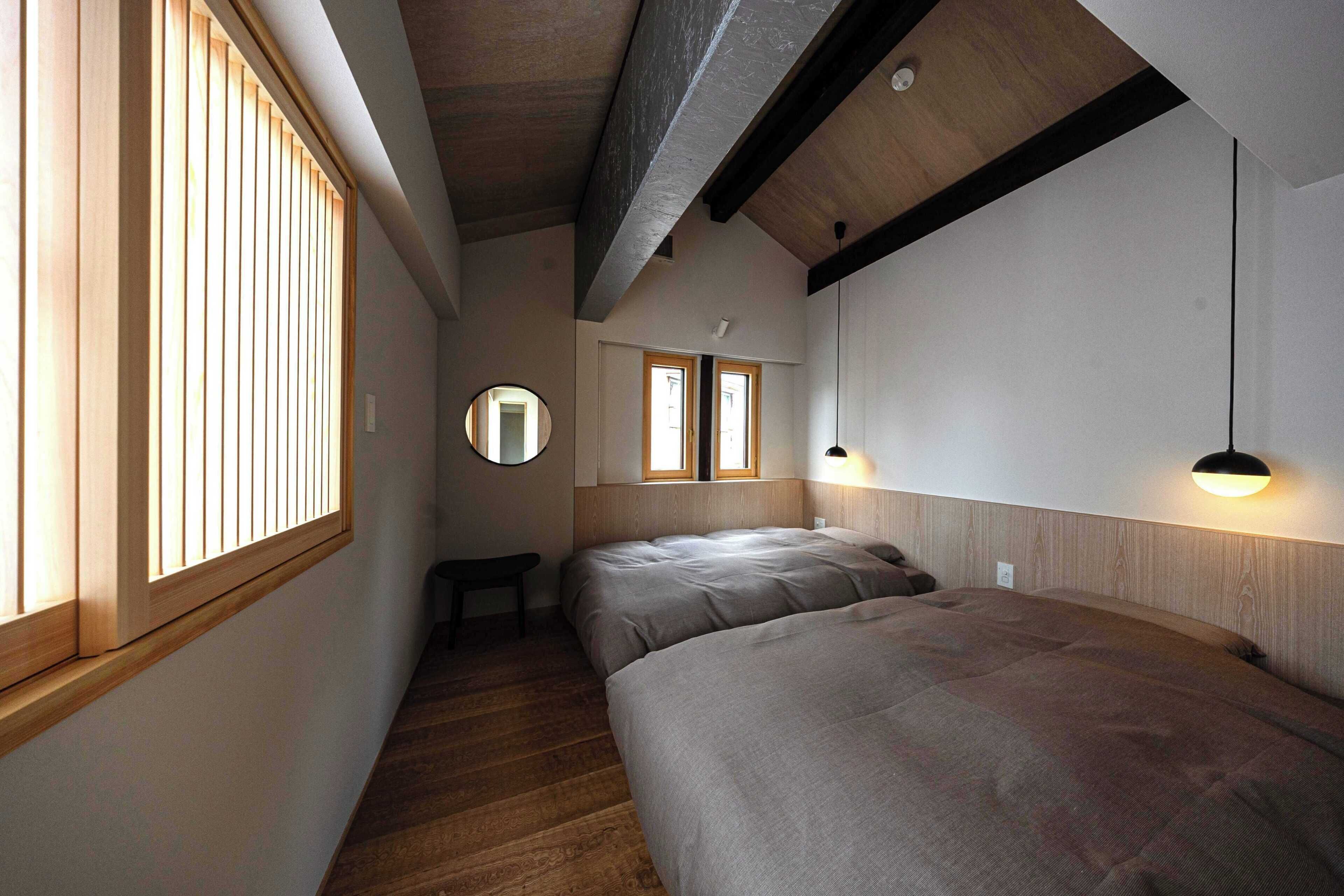 A narrow hallway with wooden flooring, two beds with grey bedding, a round mirror, and a small table.