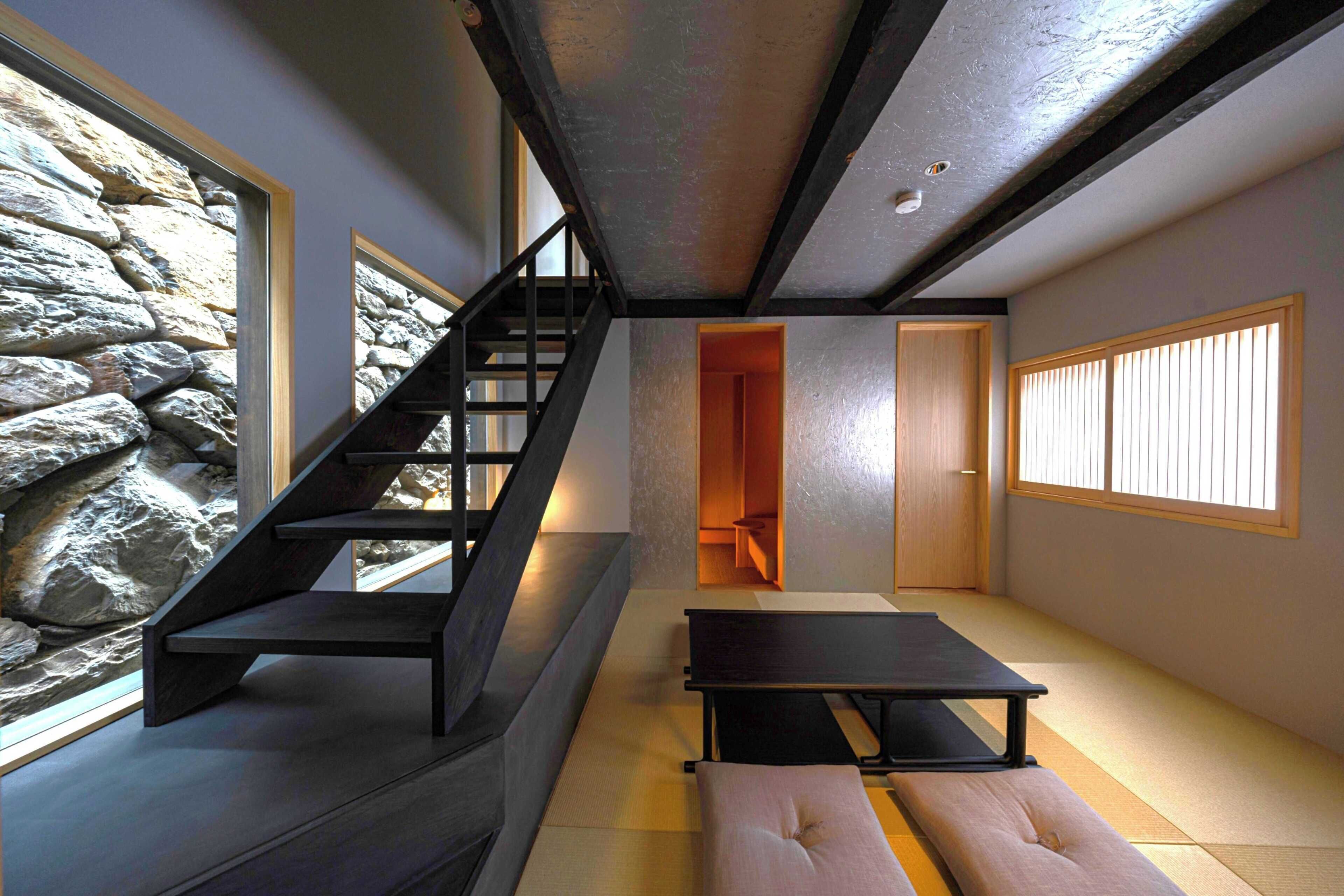 Ein modernes Interieur mit einer Steinwand, einer Treppe, einem Tatami-Boden und einer minimalistischen Möbelanordnung.
