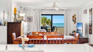 A dining area with a table and chairs, a ceiling fan, and a view of the ocean through a large window. - Gorgeous Oceanfront Retreat — Large Private Balcony, Private Beach Access & Pet-Friendly! ☀️ (Cocoa Beach)
