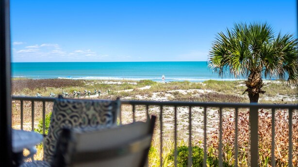 A balcony with a view of the beach, a palm tree, and a chair. - Gorgeous Oceanfront Retreat — Large Private Balcony, Private Beach Access & Pet-Friendly! ☀️ (Cocoa Beach)