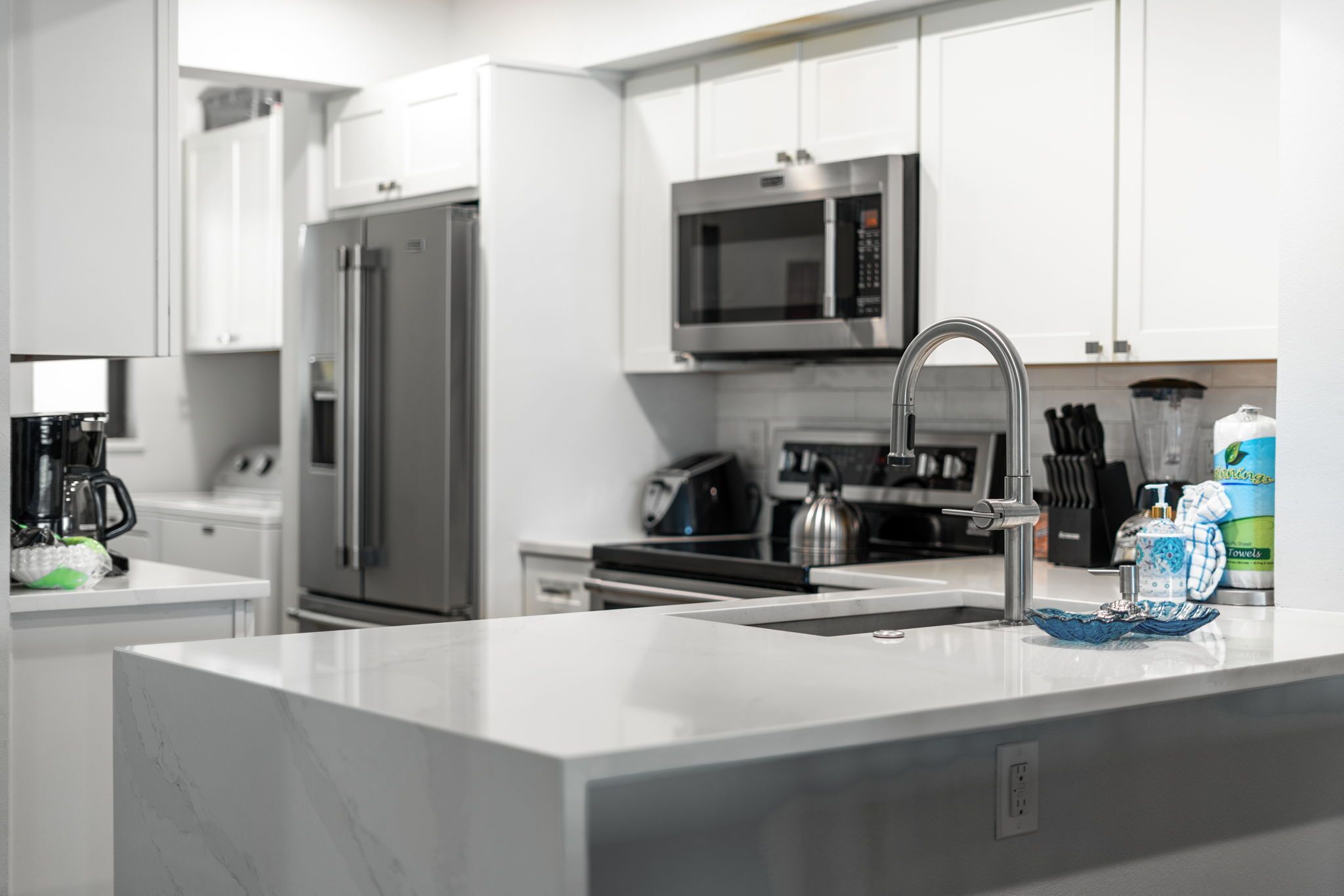 Een moderne keuken met witte kasten, roestvrijstalen apparatuur en een marmeren aanrecht.