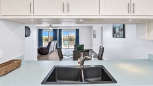 Cocina moderna con un lavamanos grande, armarios blancos y un comedor con vistas.