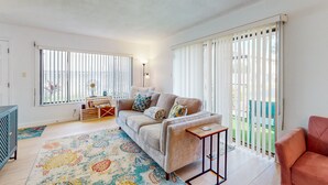 Una sala de estar con un sofá color beige, una mesita de madera, una alfombra colorida y un ventanal corredizo hacia el exterior.