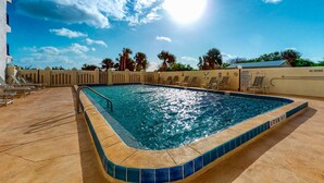 Una piscina con borde de azulejos, sillas de descanso y cielo despejado.