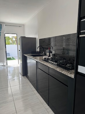 A modern kitchen with dark cabinetry, a granite countertop, a built-in stove, and a black faucet. - Fun Stay Curaçao
5 Min to Mambo Beach 2BR Home (Willemstad)