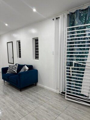 A modern living room with a blue sofa, white walls, and a large window with blinds. - Fun Stay Curaçao 
5 Min to Mambo Beach 2BR Home (Willemstad)