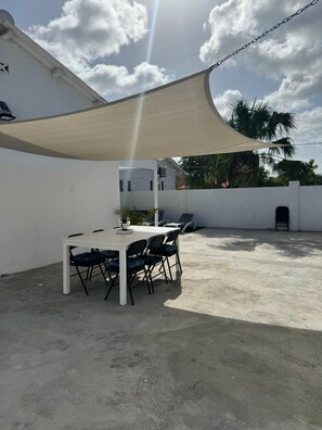 An outdoor patio with a table and chairs, a white wall, and a large shade sail. - Fun Stay Curaçao
5 Min to Mambo Beach 2BR Home (Willemstad)