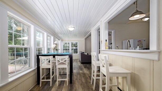 A kitchen with wooden flooring, white cabinetry, and a bar area with white chairs. - Dog-Friendly Lakeside Escape w/ Hammock & Fire Pit (Bahama)