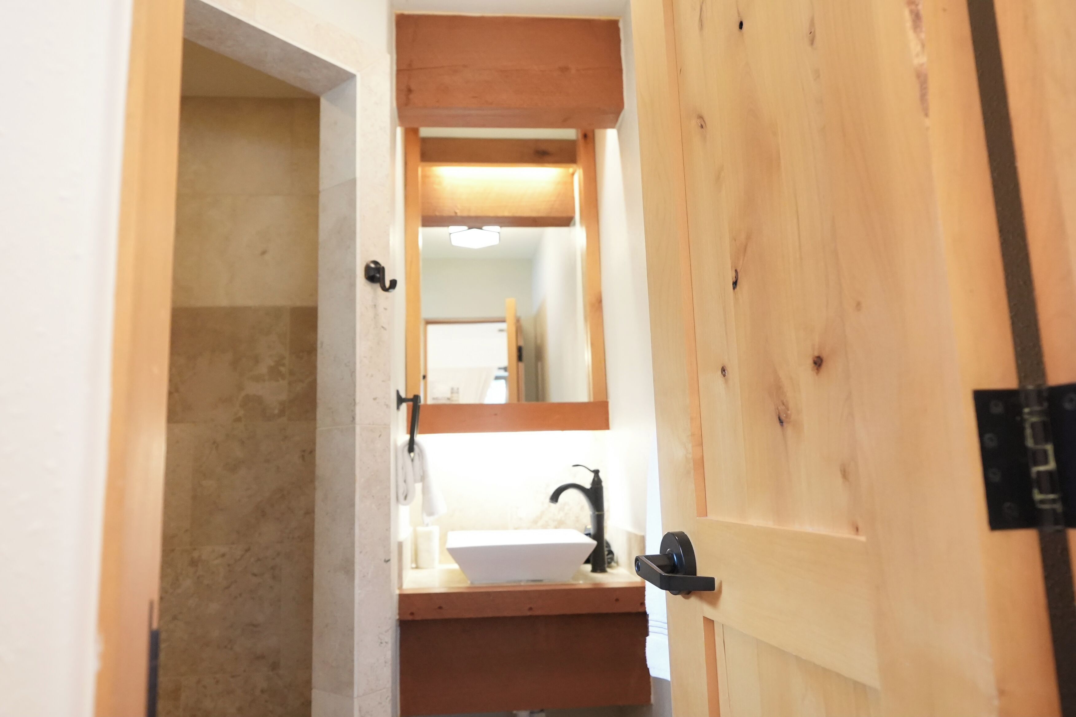 A wooden door leading to a bathroom with a white sink and a mirror above it.