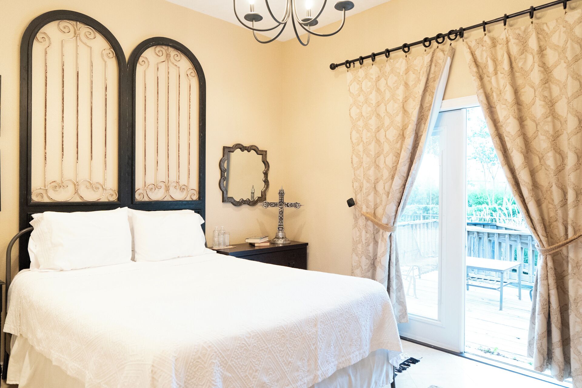 A bedroom with a bed, a nightstand, a mirror, and a view of the outdoors.