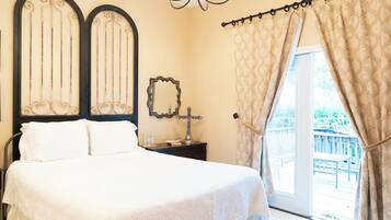 A bedroom with a bed, a nightstand, a mirror, and a view of the outdoors.