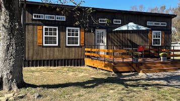 A wooden cabin with a porch, a fenced yard, and a large tree.