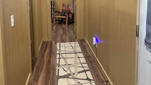 A hallway with wooden floors, a patterned rug, and various wall decorations including a mounted animal head and framed pictures. - Quiet wake cabin in Crowder (Crowder)