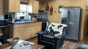 A cozy kitchen with wooden cabinets, a refrigerator, and a dining area with a leather couch and a coffee table. - Quiet wake cabin in Crowder (Crowder)