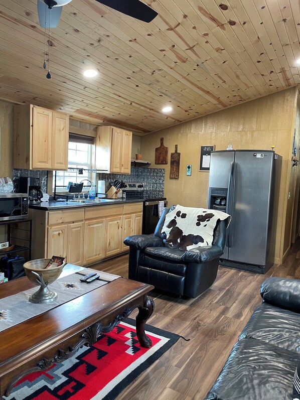 A cozy kitchen with wooden cabinets, a refrigerator, and a dining area with a leather couch and a coffee table.