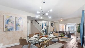 Een moderne eetruimte met een tafel met glazen blad, beklede stoelen en een moderne kroonluchter.