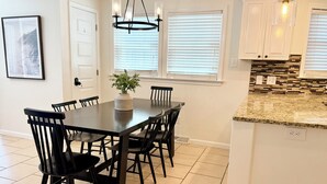 Un comedor con una mesa y sillas de madera oscura, una planta en maceta y un candelabro moderno.