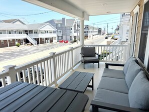 Eine überdachte Veranda mit einer Couch und Tischen, mit Blick auf eine Straße mit Gebäuden.