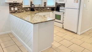 Una cocina con armarios blancos, encimera de granito, horno empotrado, microondas y refrigerador.