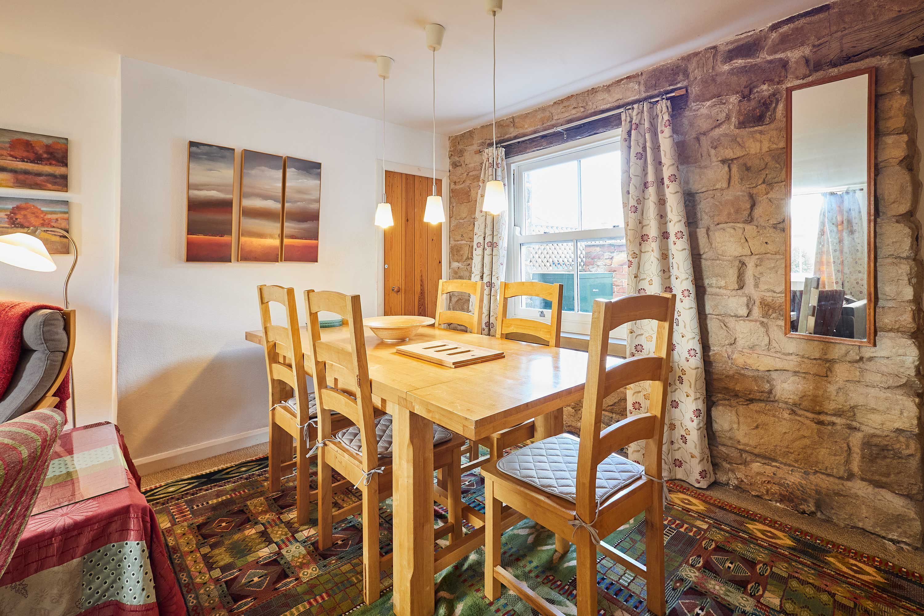 Un comedor con mesa y sillas de madera, una alfombra estampada y una pared de piedra.