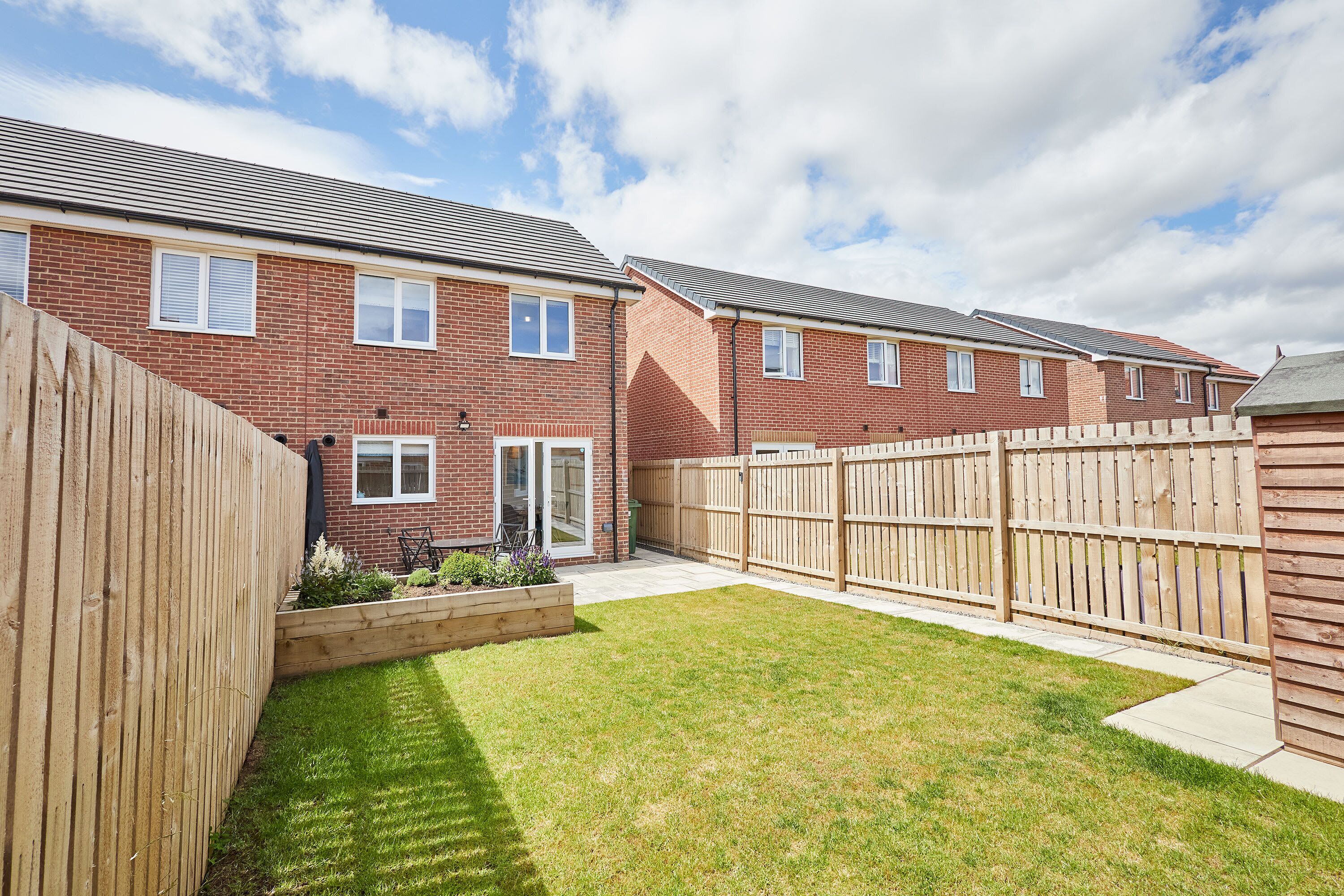 A residential property with a brick exterior, a wooden fence, and a well-maintained lawn.