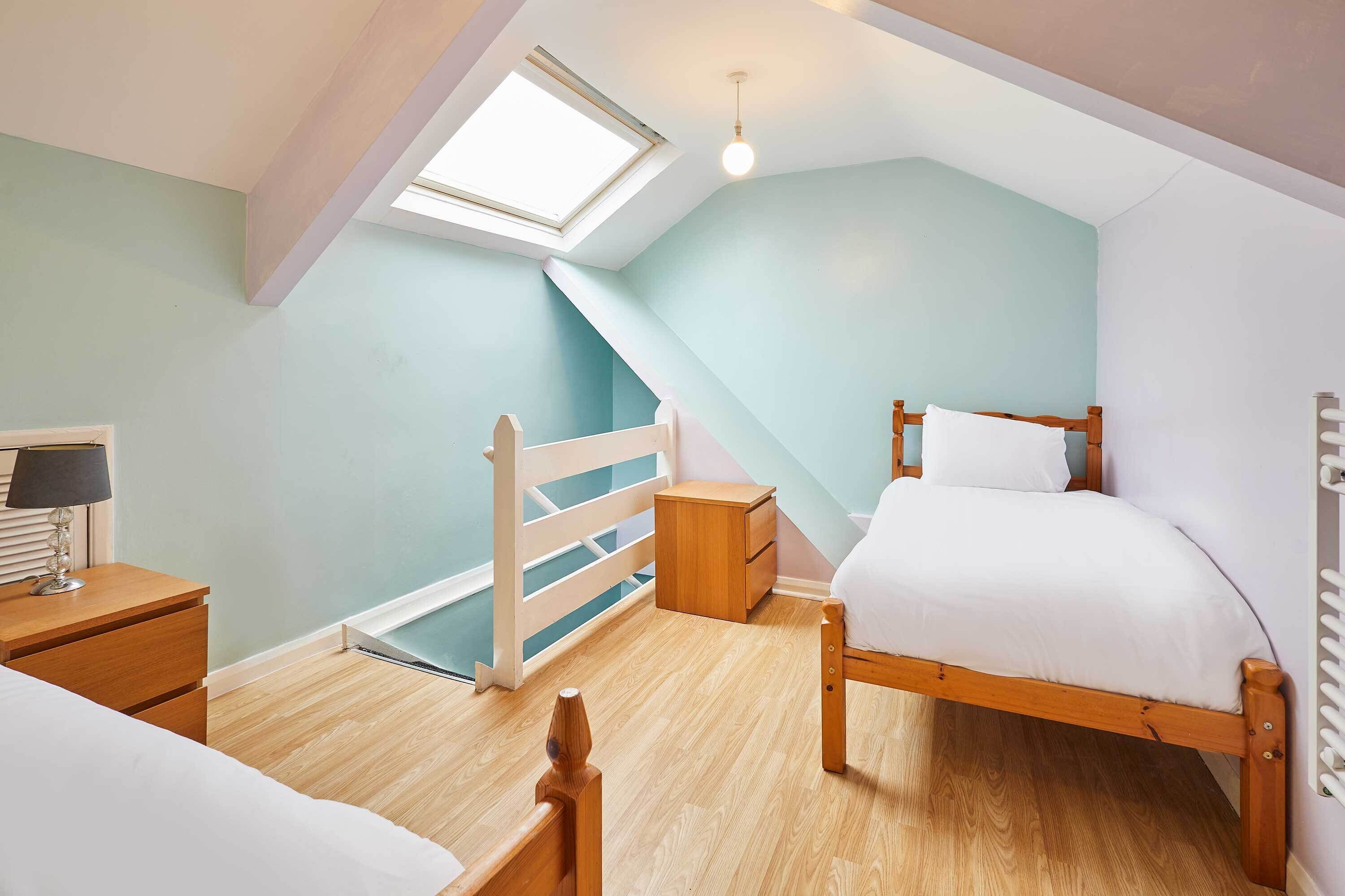 A bedroom with a skylight, wooden bed, bedside table, and a small wooden cabinet.