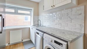 A compact kitchen with white cabinetry, a built-in sink, and a washing machine. - Host Stay Carrville Apartment (Durham)