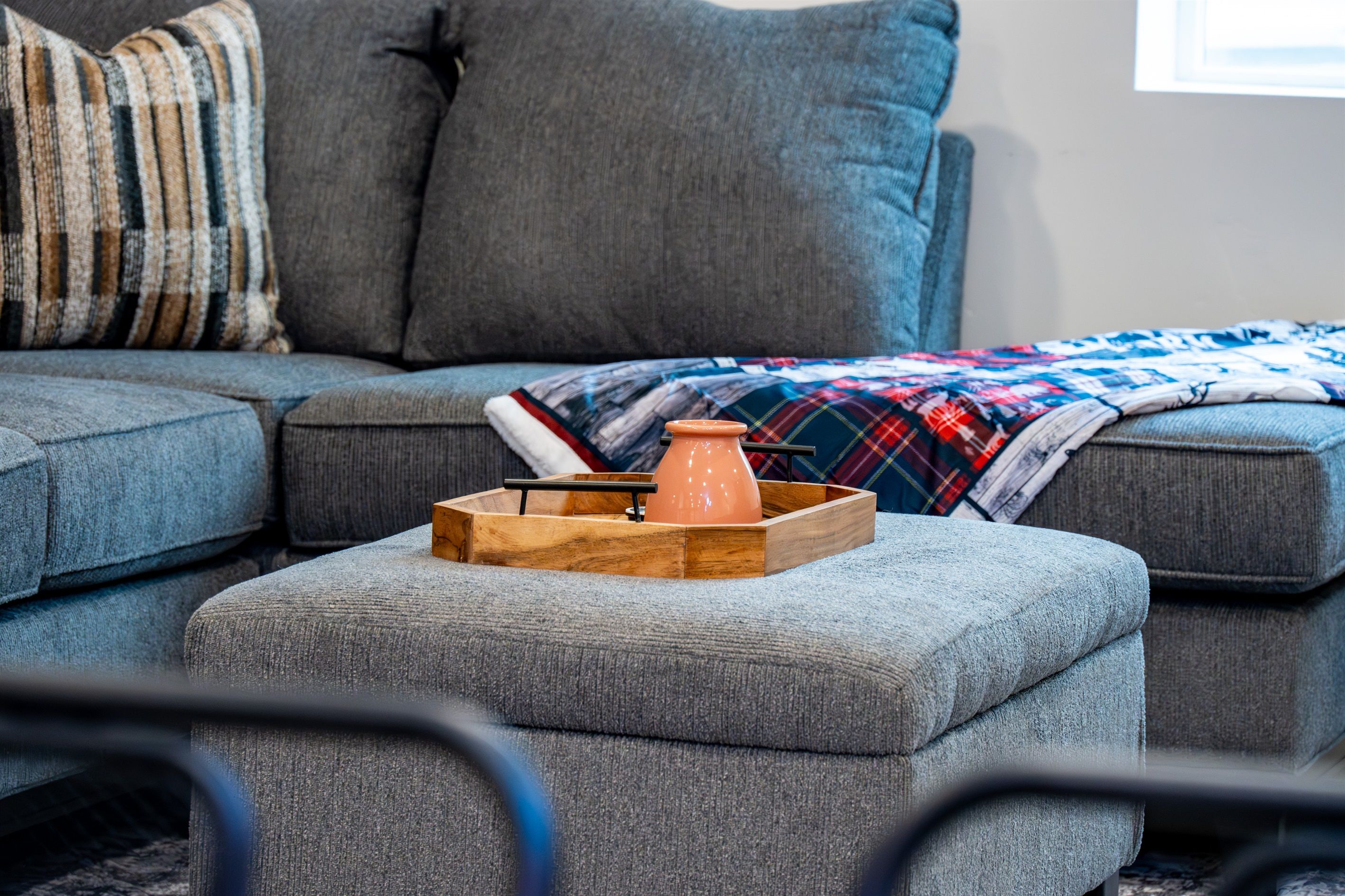 Ein graues Sofa mit einer karierten Decke und einem Holftablett mit einem Keramiktopf.