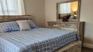 A bedroom with a wooden bed, a dresser with a mirror, and a window with curtains. - Space Coast Vacation Home — 5 Min to Kennedy Space Center & Beaches! (Titusville)
