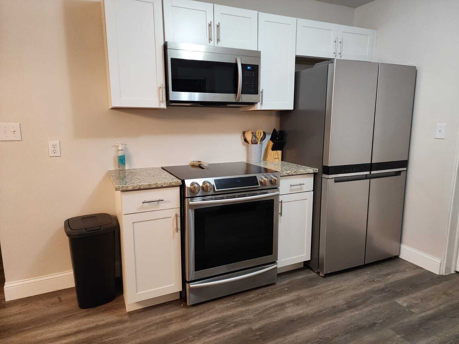 A kitchen with white cabinets, a stainless steel microwave, a double oven, and a refrigerator.