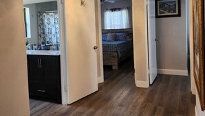 A hallway with wooden flooring, a chandelier, and a bed in the background. - Space Coast Vacation Home — 5 Min to Kennedy Space Center & Beaches! (Titusville)