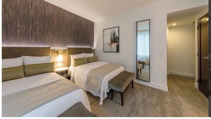 Ein Hotelzimmer mit zwei Betten, einer Bank, einer Wandleuchte und einem gerahmten Bild.