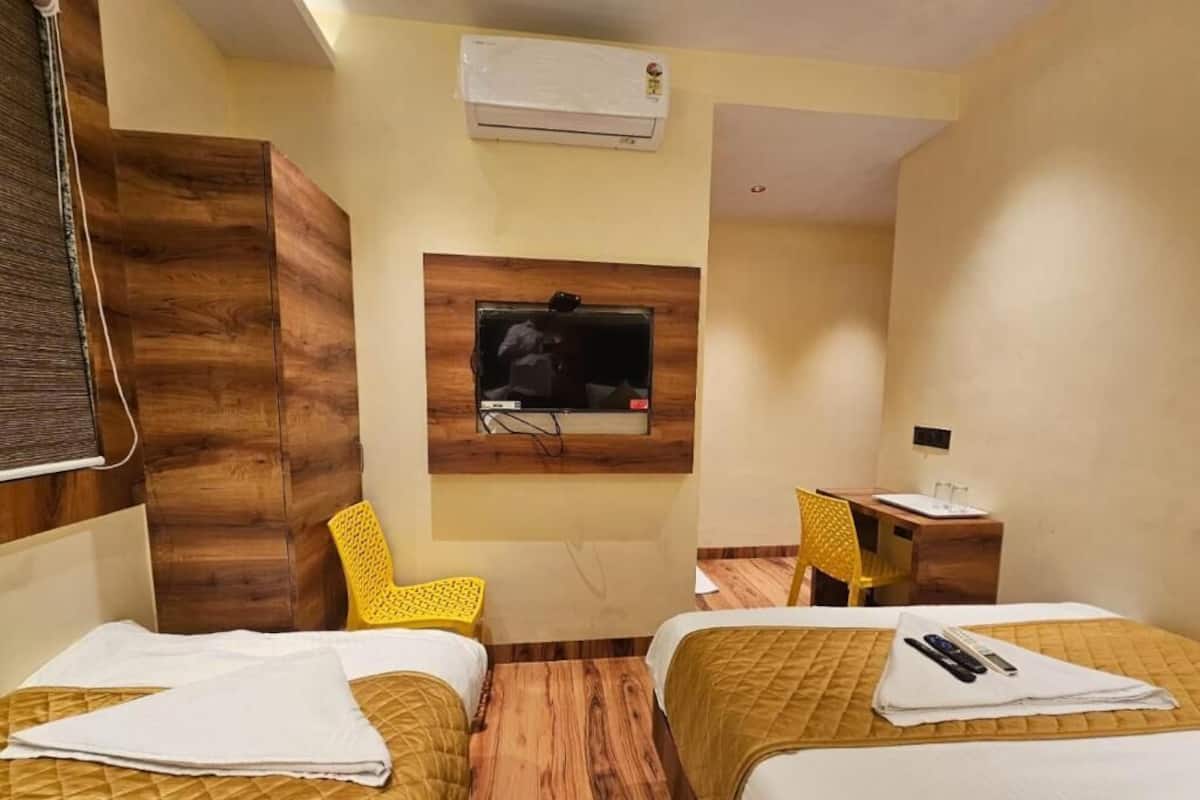 Une chambre d’hôtel avec deux lits, un téléviseur fixé au mur, un bureau avec une chaise et un appareil de climatisation.