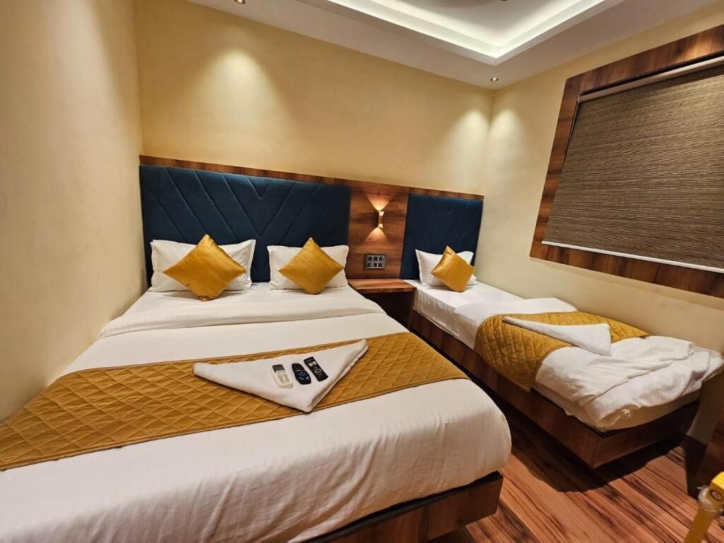 A hotel room with two beds, each with a wooden headboard, white bedding, and yellow pillows. There is a small table with a remote control and a tray.