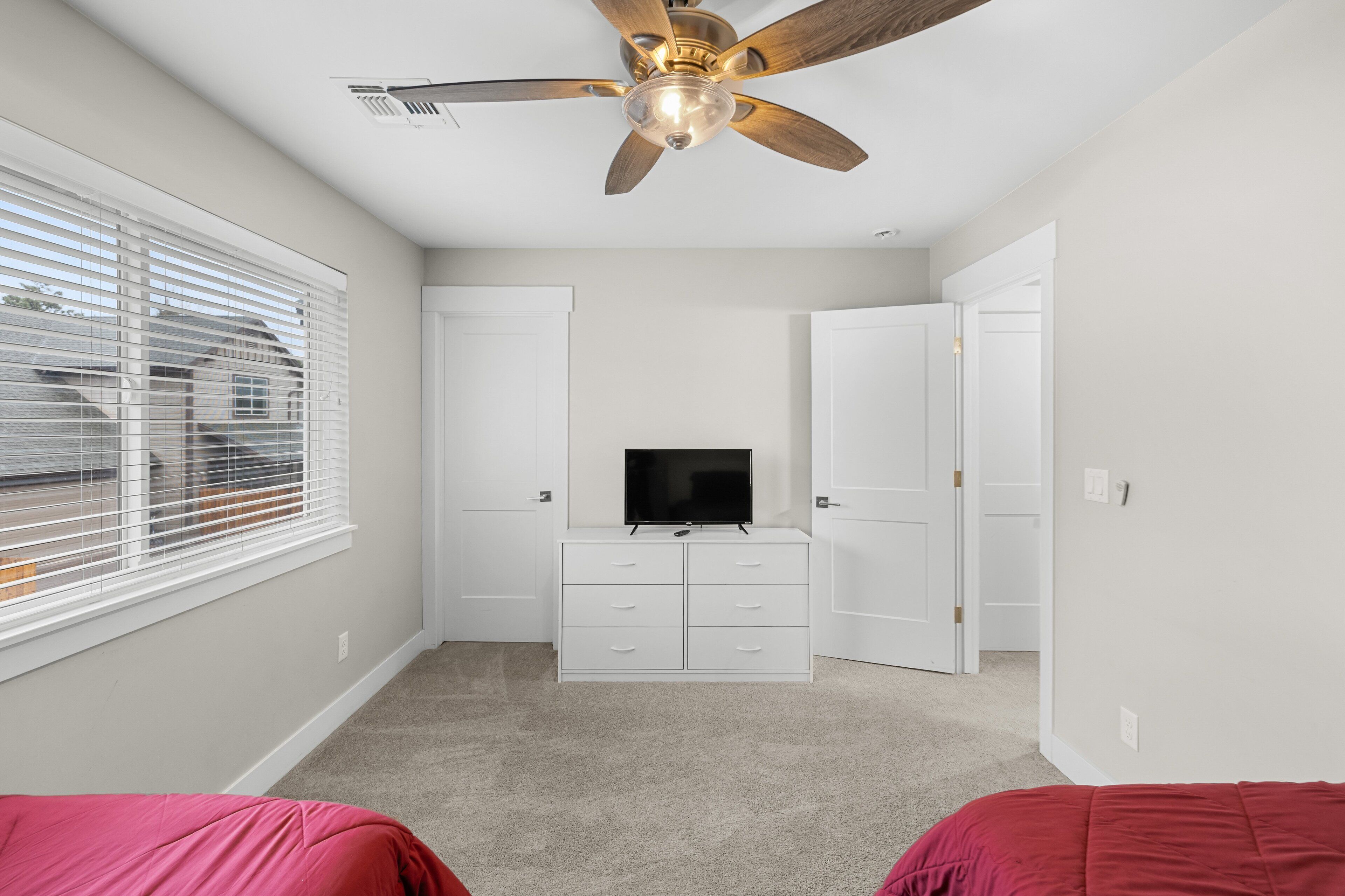 A bedroom with a ceiling fan, a TV on a dresser, and two beds.