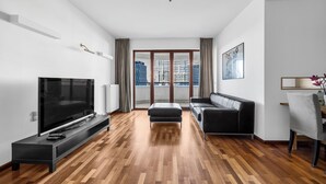 A modern living room with a flat-screen TV, a black leather sofa, and a wooden floor. - Bukowińska 22A Apartment with Terrace (Warszawa)